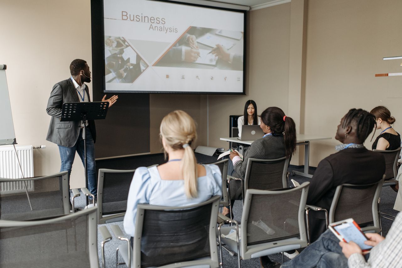 Mastering the First Impression: Your intriguing post title goes here A diverse group attends a business analysis seminar with a presenter and projection screen in a modern conference room.