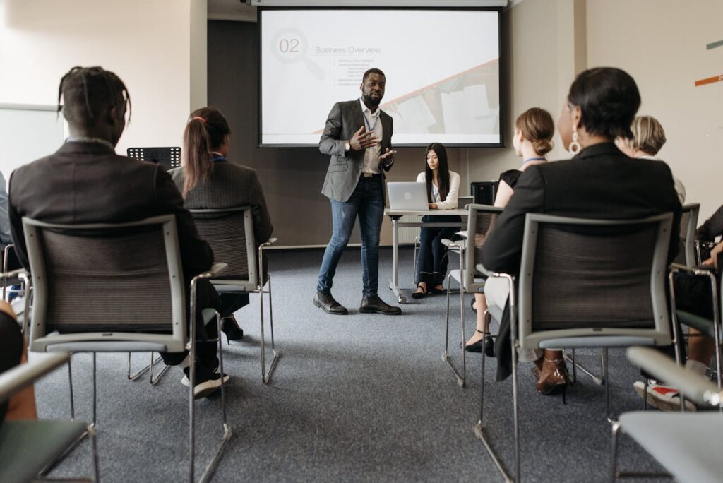 pexels photo 8761336 Diverse group attending a business seminar with a presenter and screen display.
